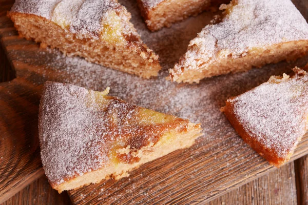 Trozos de delicioso pastel en la tabla de cortar en la mesa de madera — Foto de Stock