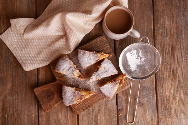 Pedaços de bolo delicioso na placa de corte com xícara de café na mesa de madeira — Fotografia de Stock