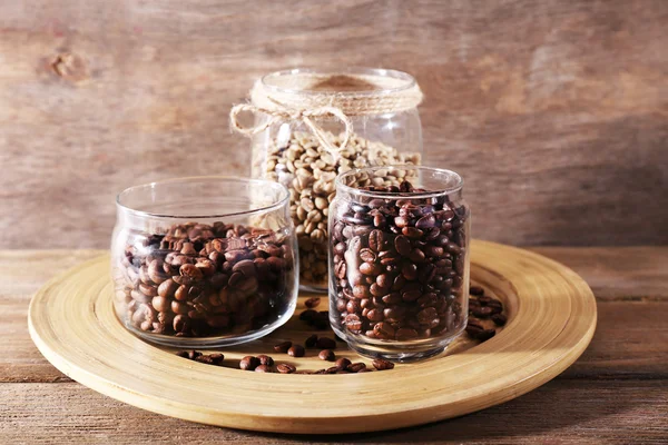 Coffee beans in jars on bamboo plate on wooden background — Stock Photo, Image