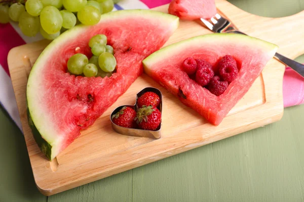 Fresh juicy watermelon slice  with cut out heart shape, filled fresh berries, on cutting board, on wooden background — Stock Photo, Image