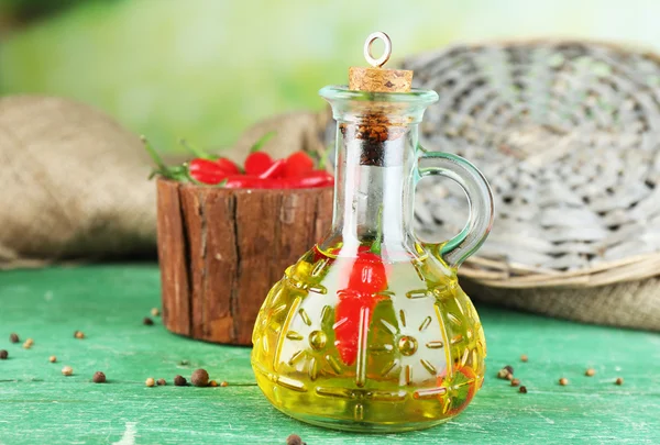 自制天然橄榄油充满红辣椒在瓶上彩色木桌前，在明亮的背景上 — 图库照片