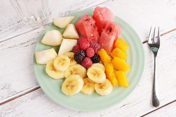 Frutta affettata e bacche su piatto con bicchiere d'acqua su tavolo di legno — Foto Stock