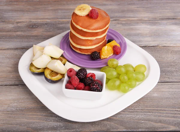 Блинчик с фруктами и ягодами на тарелке на деревянном столе — стоковое фото