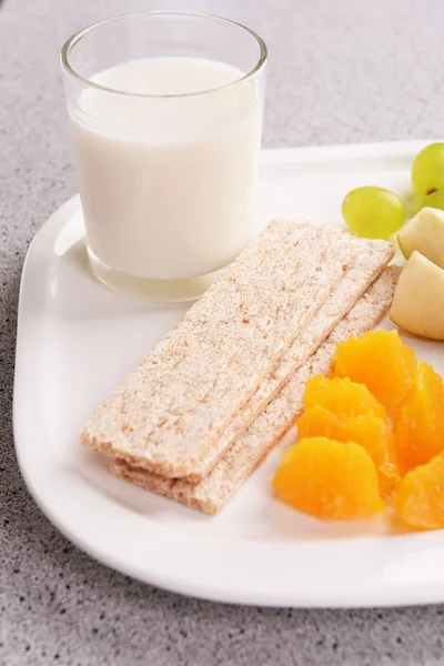 Obstscheiben mit Knäckebrot und Glas Milch auf Teller auf dem Tisch in Großaufnahme — Stockfoto