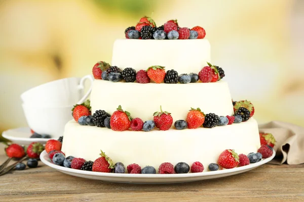 Beau gâteau de mariage avec des baies sur table en bois, sur fond de nature — Photo