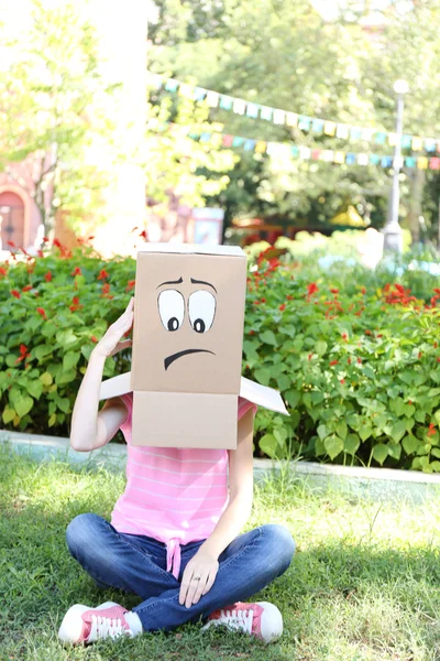 Mulher com caixa de papelão na cabeça com rosto triste, ao ar livre — Fotografia de Stock