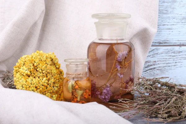 Bottles of herbal tincture and dried herbs on a napkin on wooden background in front of curtain — Stock Photo, Image