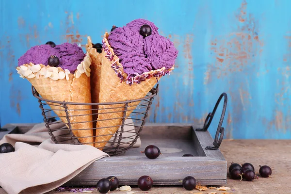 Gustoso gelato con bacche in coni di cialde su sfondo blu in legno — Foto Stock