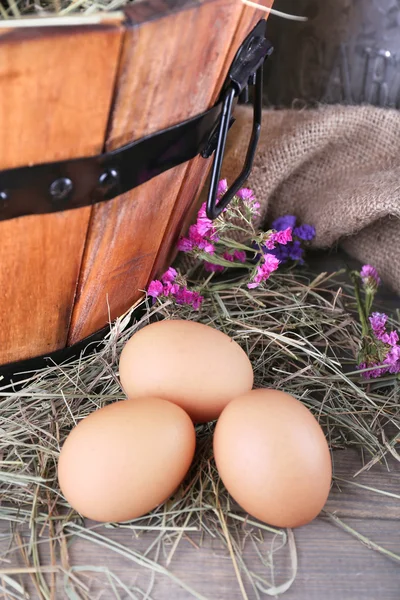 Big round basket with dried grass and fresh eggs on sacking background — Stock Photo, Image