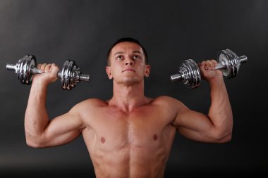 yakışıklı genç kaslı sporcu, koyu arka plan üzerinde egzersiz halter ile yürütmek