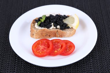 Siyah havyar ve tereyağı ekmek üzerinde koyu kumaş arka plan üzerinde tabakta domates ile