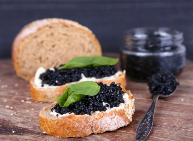 Tereyağı ve ahşap masa üzerinde koyu arka plan üzerinde siyah havyar ile ekmek dilimleri