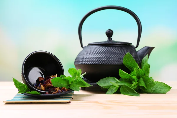 Bule tradicional chinês com folhas de hortelã fresca e pétalas de hibisco secas na mesa de madeira, no fundo brilhante — Fotografia de Stock