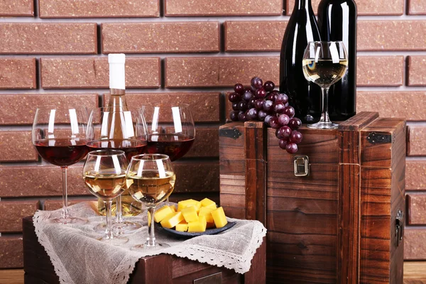 Flaschen und Gläser mit Wein, Käse und reifen Trauben auf dem Tisch vor Backsteinmauer Hintergrund — Stockfoto