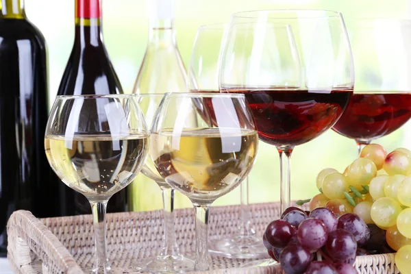 Flaschen und Gläser mit Wein und reifen Trauben auf dem Tisch vor natürlichem Hintergrund — Stockfoto