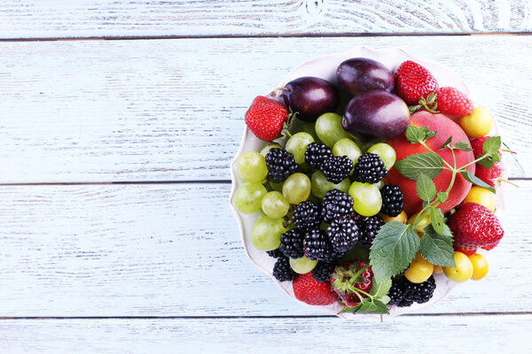 Different berries and fruits in plate on wooden table close-up