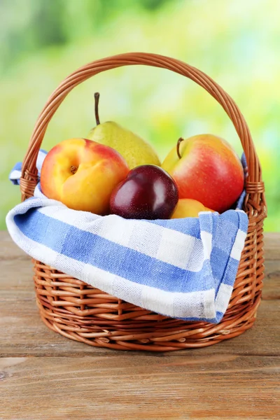 Surtido de frutas jugosas en canasta de mimbre sobre mesa, sobre fondo brillante — Foto de Stock