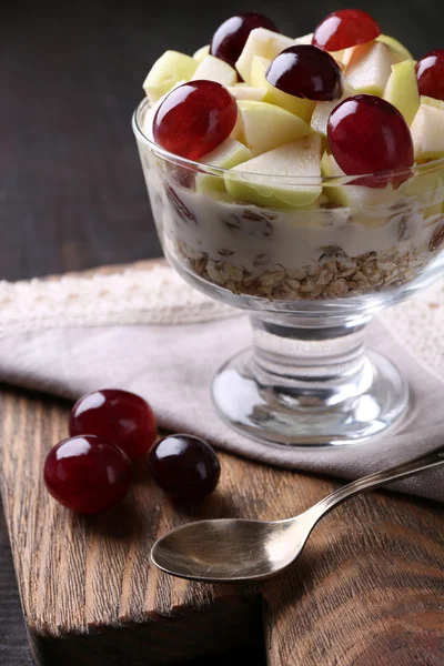 Gezond ontbijt - yoghurt met vers druif en apple segmenten en muesli geserveerd in glazen kom, op houten achtergrond — Stockfoto