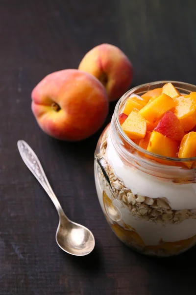 健康-酸奶鲜桃和牛奶什锦早餐在玻璃罐中，木制的背景上 — 图库照片