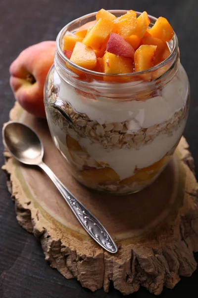 Colazione sana - yogurt con pesca fresca e muesli servito in barattolo di vetro, su sfondo di legno — Foto Stock