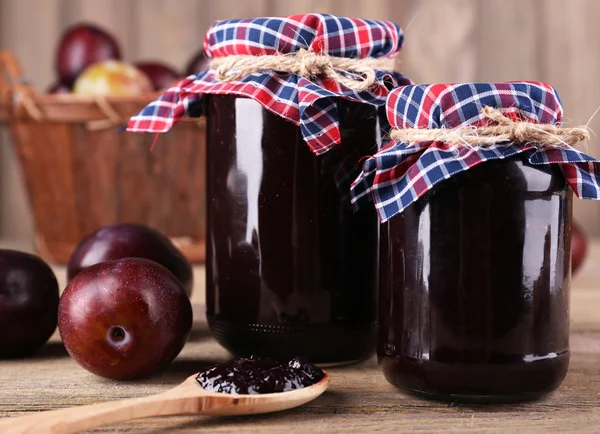 Tasty plum jam in jars and plums on wooden table — Stock Photo, Image