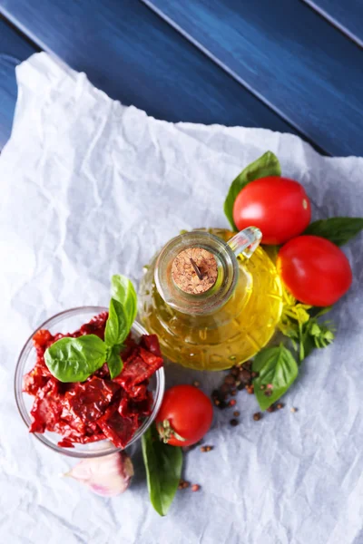 Sun dried tomatoes in glass jar, olive oil in glass bottle, basil leaves on color wooden background — Stock Photo, Image