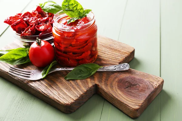 Suszonymi pomidorami w szklanym słoiku, bazylii na deski do krojenia, na tle drewniane — Zdjęcie stockowe