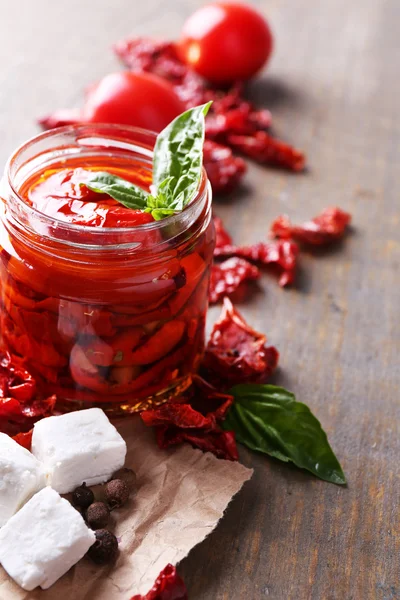 Suszone pomidory w szklanym słoiku, liście bazylii i ser feta na drewniane tła kolor — Zdjęcie stockowe