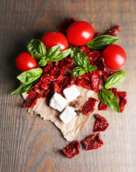 Tomates secos y frescos al sol, hojas de albahaca y queso feta sobre fondo de madera de color —  Fotos de Stock