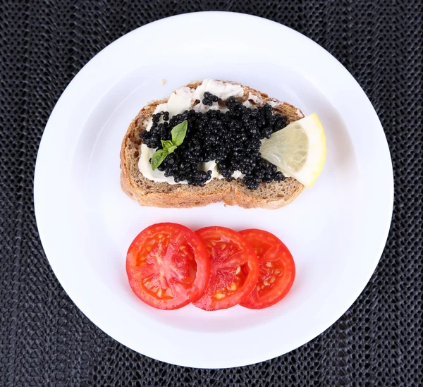 Caviar negro y mantequilla en pan con tomate en plato sobre fondo de tela oscura —  Fotos de Stock