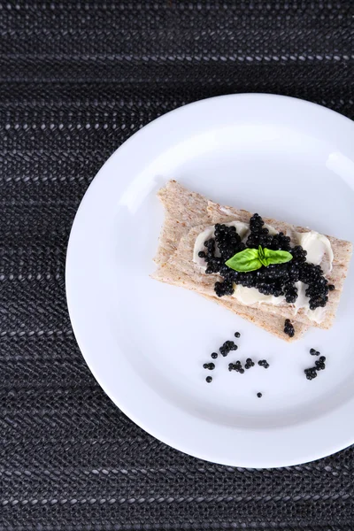 Slices of bread with butter and black caviar on plate on dark fabric background — Stock Photo, Image