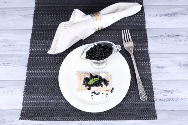 Slice of bread with butter and black caviar on plate on napkin on wooden background — Stock Photo, Image