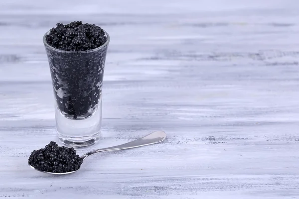 Glass and spoon of black caviar on grey wooden background — Stock Photo, Image