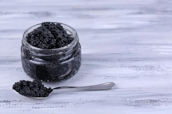 Tarro de vidrio y cuchara de caviar negro sobre fondo de madera gris — Foto de Stock