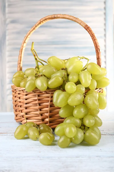 Uvas maduras en canasta de mimbre sobre mesa de madera sobre fondo claro — Foto de Stock