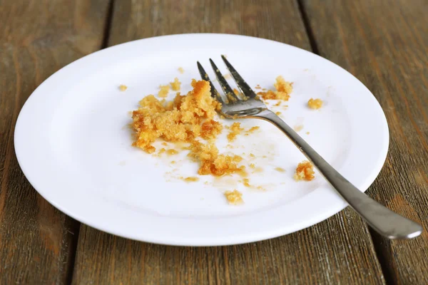 Dirty empty plate with fork on wooden table — Stock Photo, Image