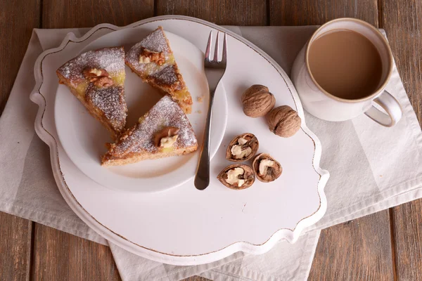 Pedaços de bolo delicioso com nozes em pé de madeira na mesa de perto — Fotografia de Stock