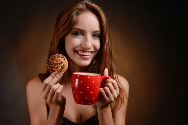 Mooi meisje met kop koffie op bruine achtergrond — Stockfoto