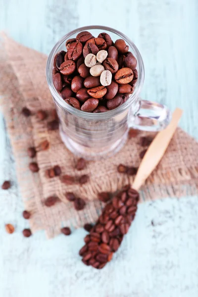 Sklo a lžičku s kávová zrna v žíně na modré dřevěné pozadí — Stock fotografie