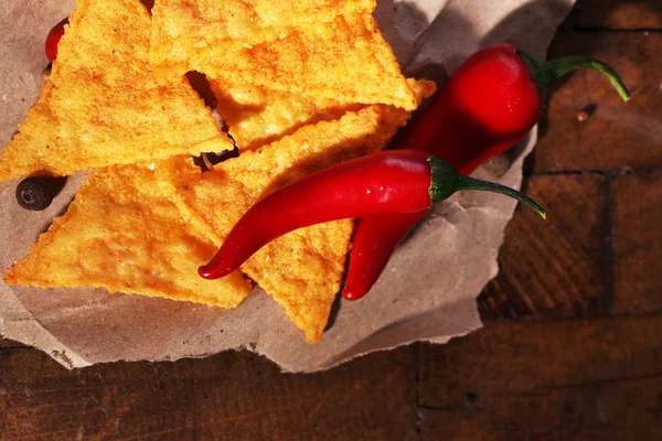 Nachos saborosos e pimenta no papel, no fundo de madeira — Fotografia de Stock