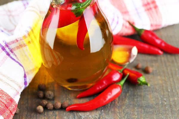 Aceite de oliva infundido natural casero con chiles rojos y especias en jarra de vidrio sobre fondo de madera — Foto de Stock