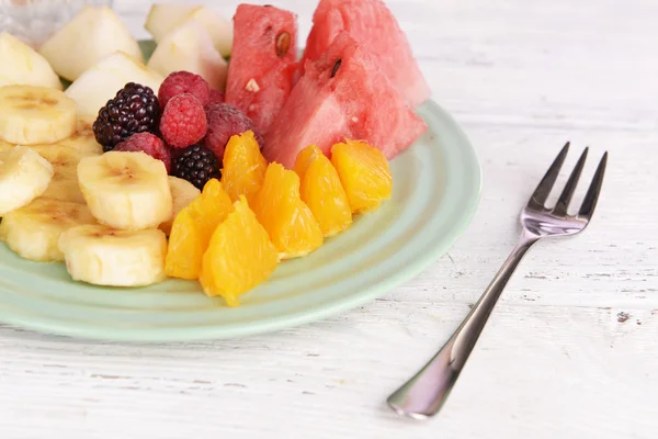 Frutas y bayas en rodajas en plato sobre mesa de madera —  Fotos de Stock