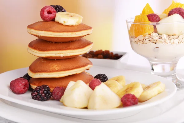 Pancake dengan buah-buahan di piring dan muesli di atas meja dengan latar belakang cerah — Stok Foto