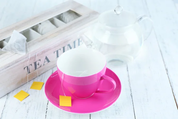 Cup en theepot met thee zakjes op houten tafel close-up — Stockfoto