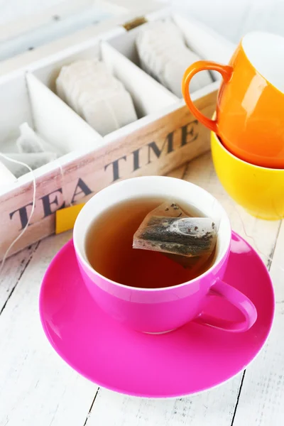 Taza con bolsitas de té y té en primer plano de mesa de madera —  Fotos de Stock