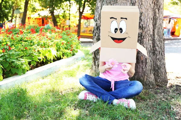 Vrouw met kartonnen doos op haar hoofd met blij gezicht, bedrijf bloem, buitenshuis — Stockfoto