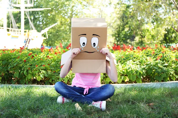 Femme avec boîte en carton sur la tête avec visage triste et crème glacée sur l'herbe verte, à l'extérieur — Photo