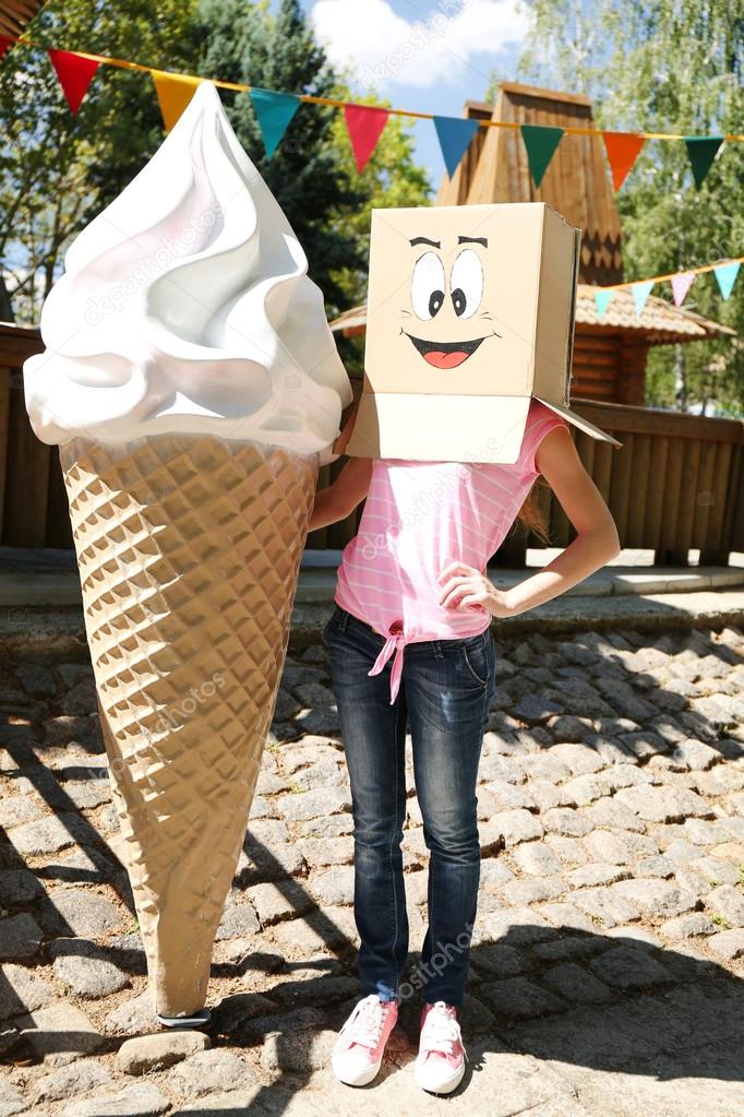 Woman with cardboard box on her head with happy face near big ice cream, outdoors