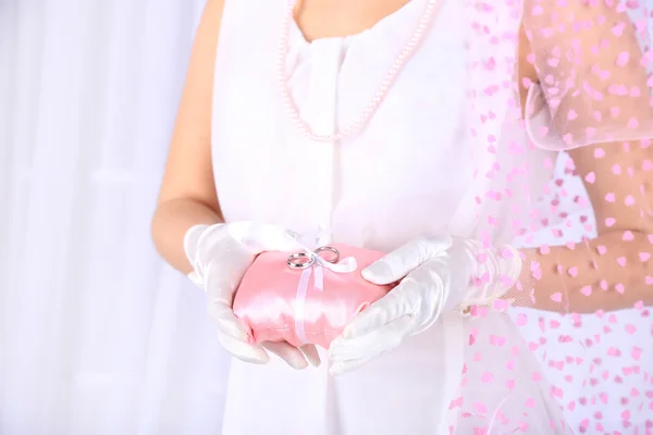 Bride in white dress and gloves holding decorative pillow with wedding rings, close-up — Stock Photo, Image