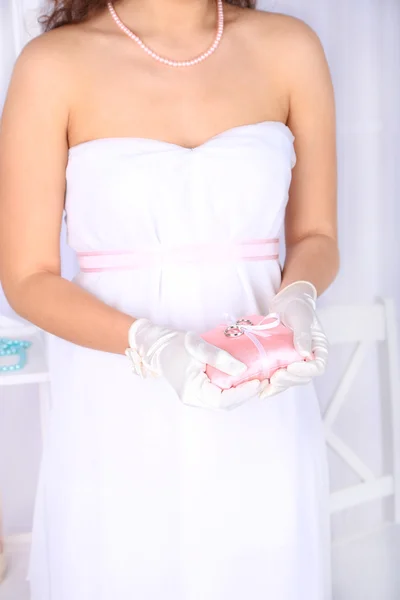 Mariée en robe blanche et gants tenant un oreiller décoratif avec des alliances, gros plan, sur fond clair — Photo